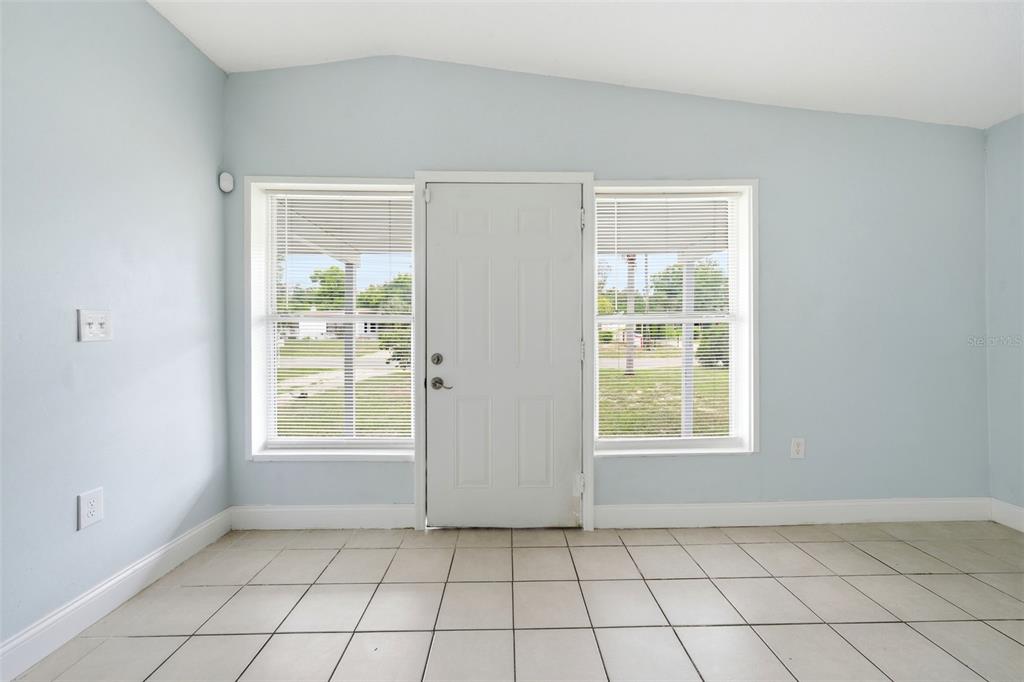 A room with light blue walls, white tile flooring, a central door, and two windows — 1311 HILLCREST DRIVE, DAYTONA BEACH, FL