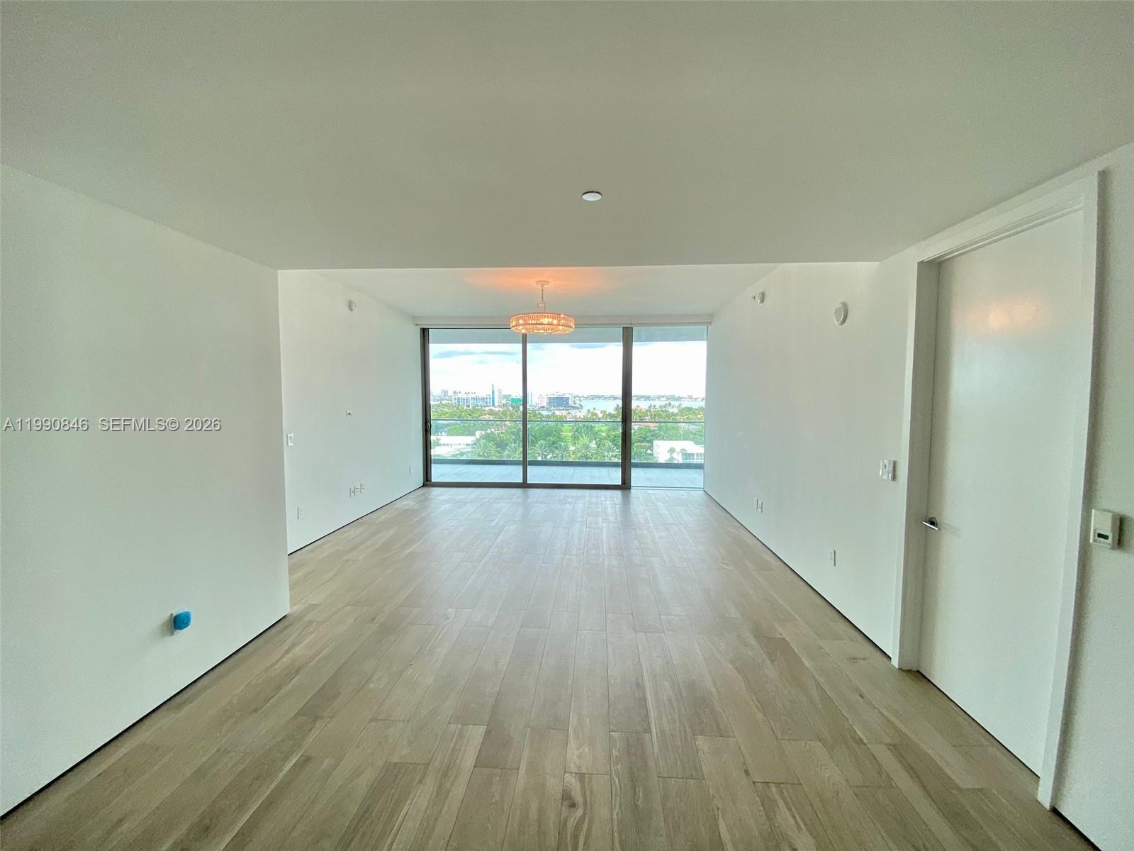 An empty room features light wood-look flooring, white walls, and floor-to-ceiling windows with a view — 10203 Collins Ave # 905, Bal Harbour FL 33154, BAL HARBOUR, FL