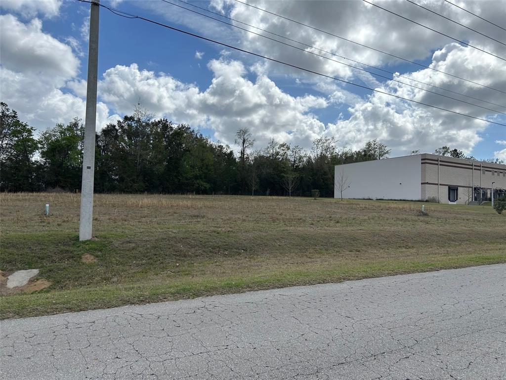 A vacant, grassy lot sits next to a large industrial building under a cloudy sky — NW 104TH TERRACE, ALACHUA, FL