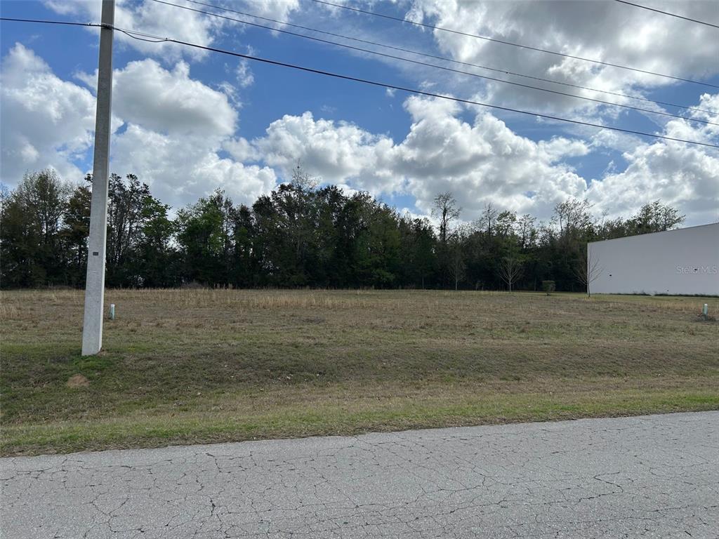 A vacant, grassy lot sits beside a paved road and a large white building — NW 104TH TERRACE, ALACHUA, FL