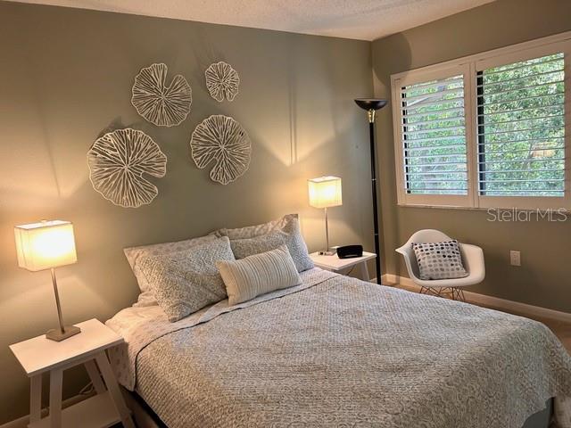 A bedroom features a bed with patterned bedding, wall art, two lamps, and a chair — 1680 BROOKHOUSE CIRCLE UNIT BR209, SARASOTA, FL