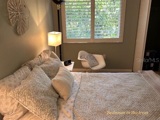 A bedroom features a bed with patterned bedding, a white chair, and a window with shutters — 1680 BROOKHOUSE CIRCLE UNIT BR209, SARASOTA, FL