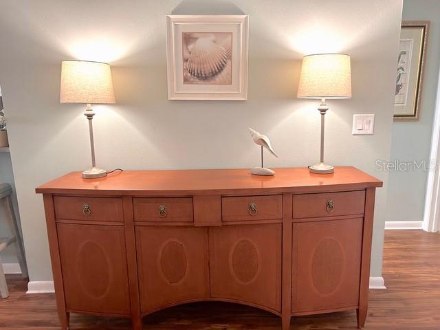 A wooden sideboard with two lamps and a framed shell print sits against a wall — 1680 BROOKHOUSE CIRCLE UNIT BR209, SARASOTA, FL