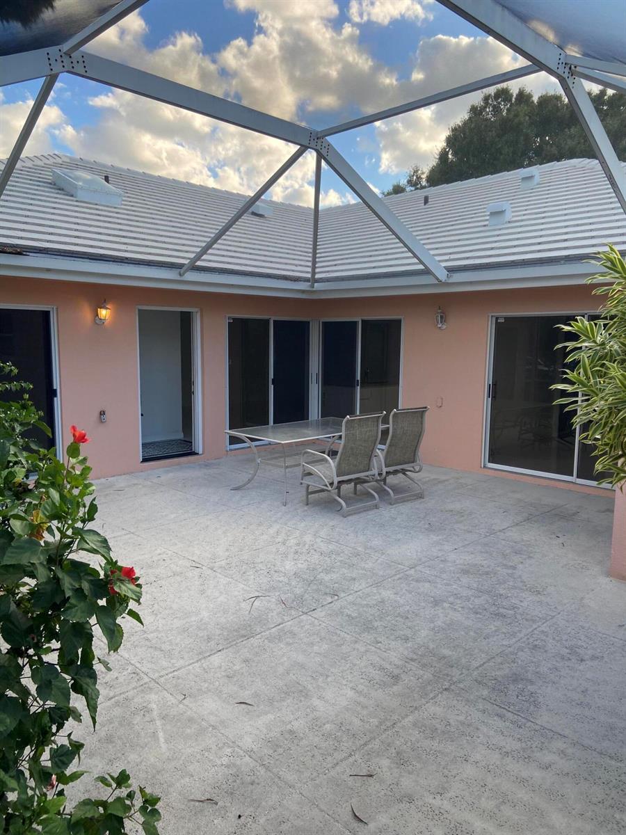 A screened-in patio features a concrete floor, a glass-top table, and two chairs — 2102 Appleton Court, Palm Beach Gardens FL 33403, PALM BEACH GARDENS, FL