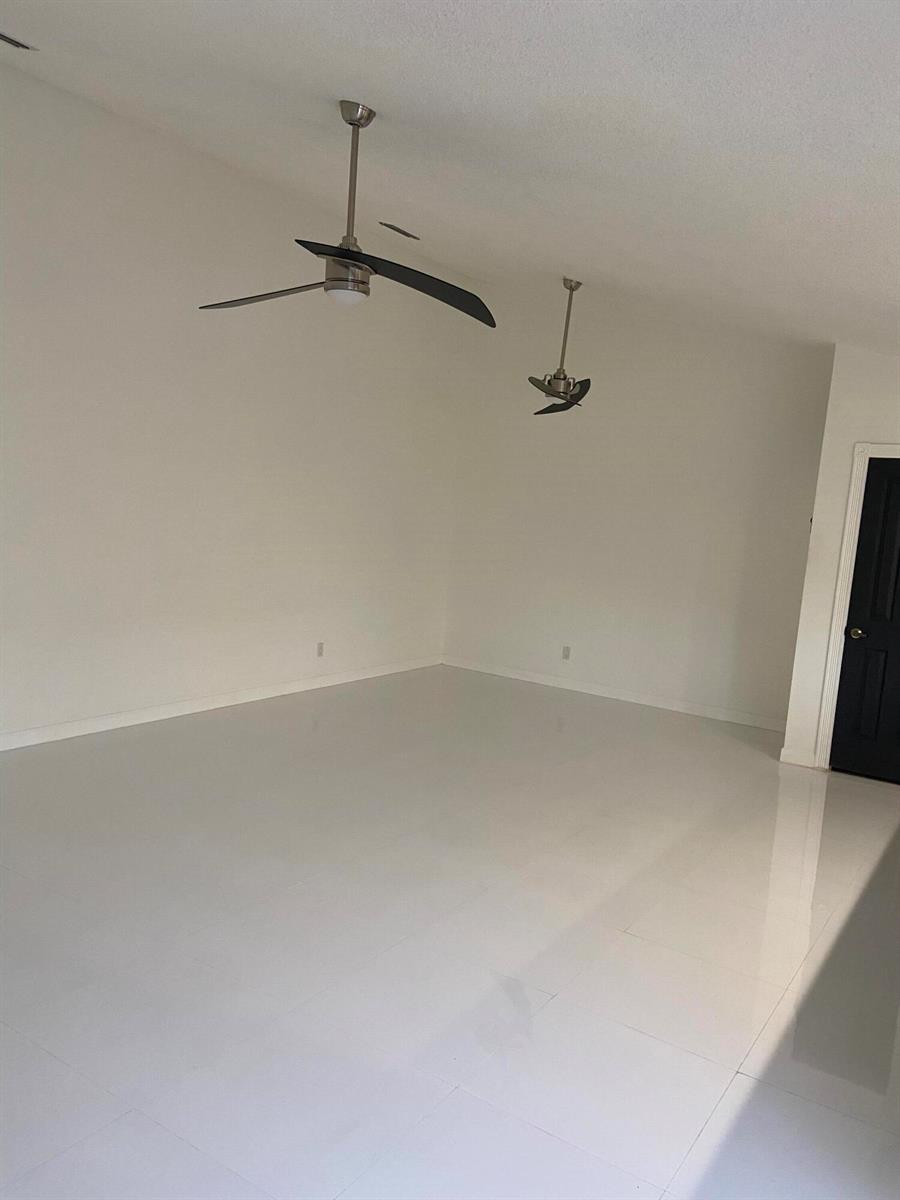 An empty room features white tile flooring, white walls, and two ceiling fans — 2102 Appleton Court, Palm Beach Gardens FL 33403, PALM BEACH GARDENS, FL