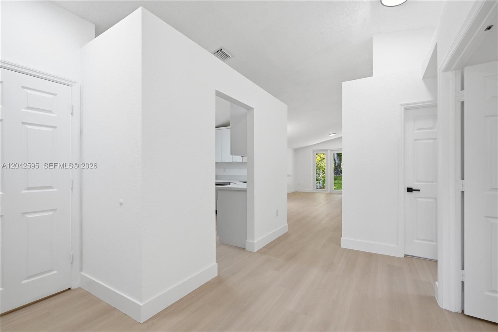 A bright hallway with light wood-look flooring leads to an open living area and kitchen — 4114 Sapphire St, Weston FL 33331, WESTON, FL