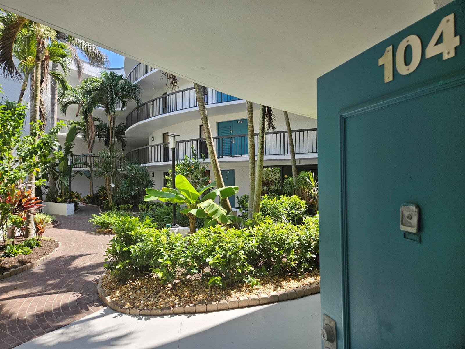 A view from a doorway labeled 104 looking out onto a tropical courtyard and building — 1357 NE Ocean # 104, Stuart FL 34996, STUART, FL