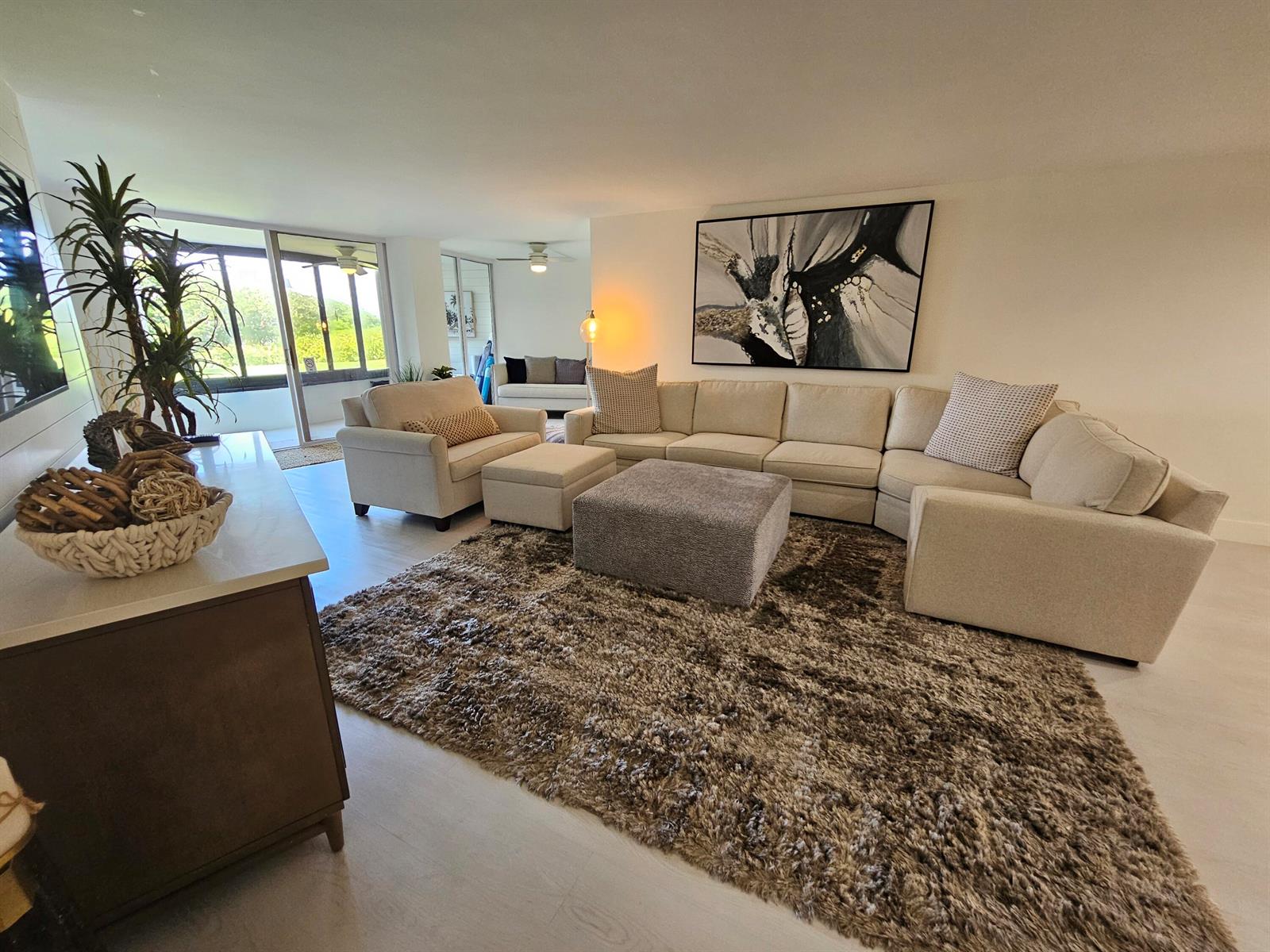 A spacious living room features a large sectional sofa, a shaggy rug, and sliding glass doors — 1357 NE Ocean # 104, Stuart FL 34996, STUART, FL