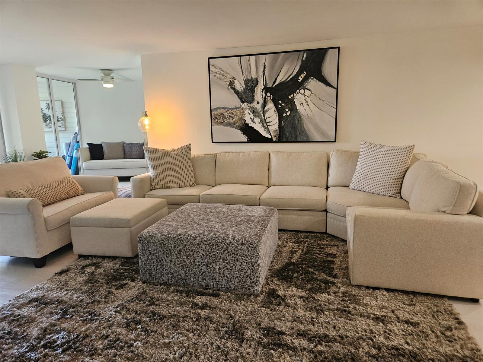 A living room features a large beige sectional, a patterned ottoman, and abstract wall art — 1357 NE Ocean # 104, Stuart FL 34996, STUART, FL