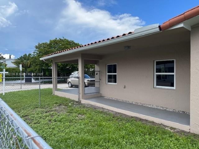 The exterior of a house features a covered patio, a chain-link fence, and lawn — 200 NE 44th St # 0, Miami FL 33137, MIAMI, FL