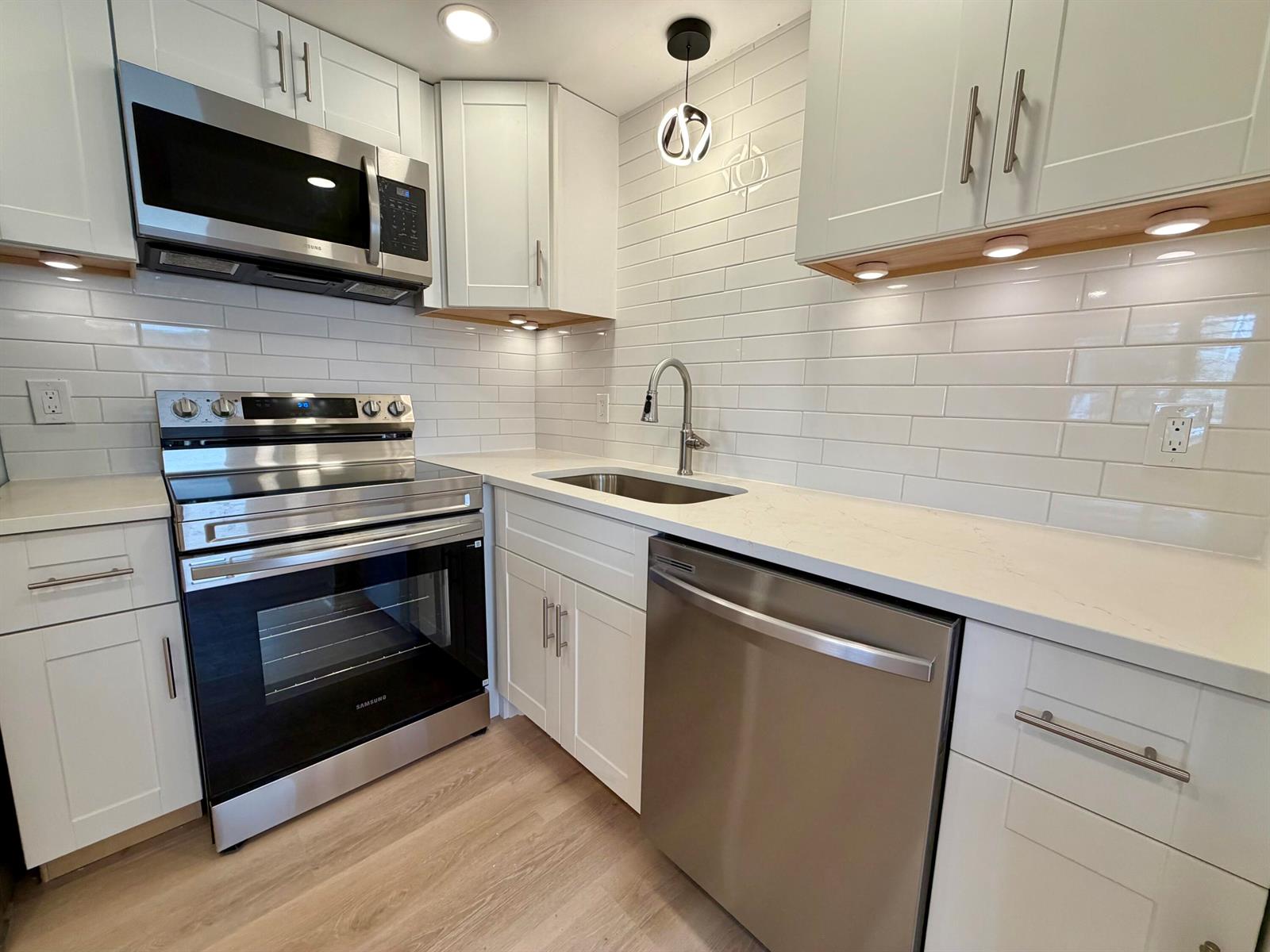 A modern kitchen features white cabinets, stainless steel appliances, a subway tile backsplash, and countertops — 207 Tuscany D # 207, Delray Beach FL 33446, DELRAY BEACH, FL