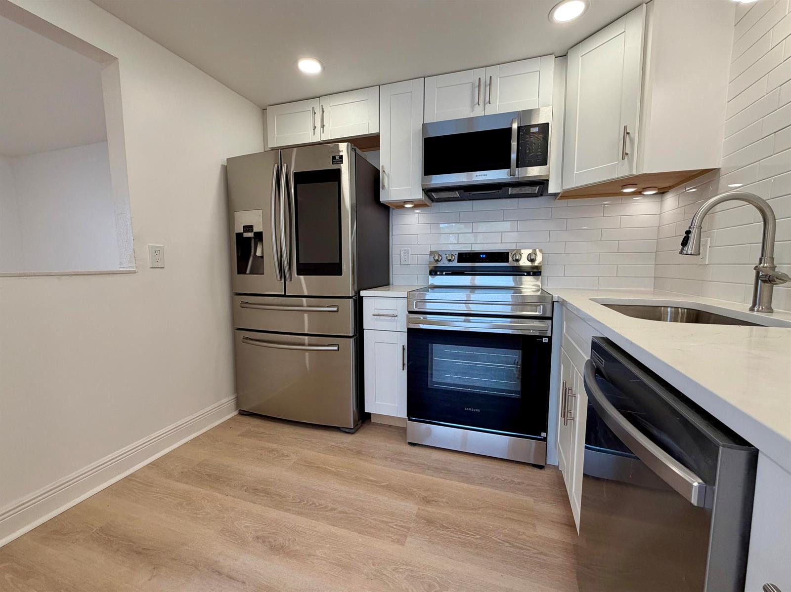A kitchen features white cabinets, stainless steel appliances, a subway tile backsplash, and light flooring — 207 Tuscany D # 207, Delray Beach FL 33446, DELRAY BEACH, FL