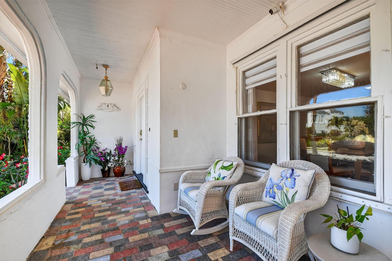 A covered porch features a multicolored brick floor, white walls, and two wicker rocking chairs — 328 Monroe Drive, West Palm Beach FL 33405, WEST PALM BEACH, FL