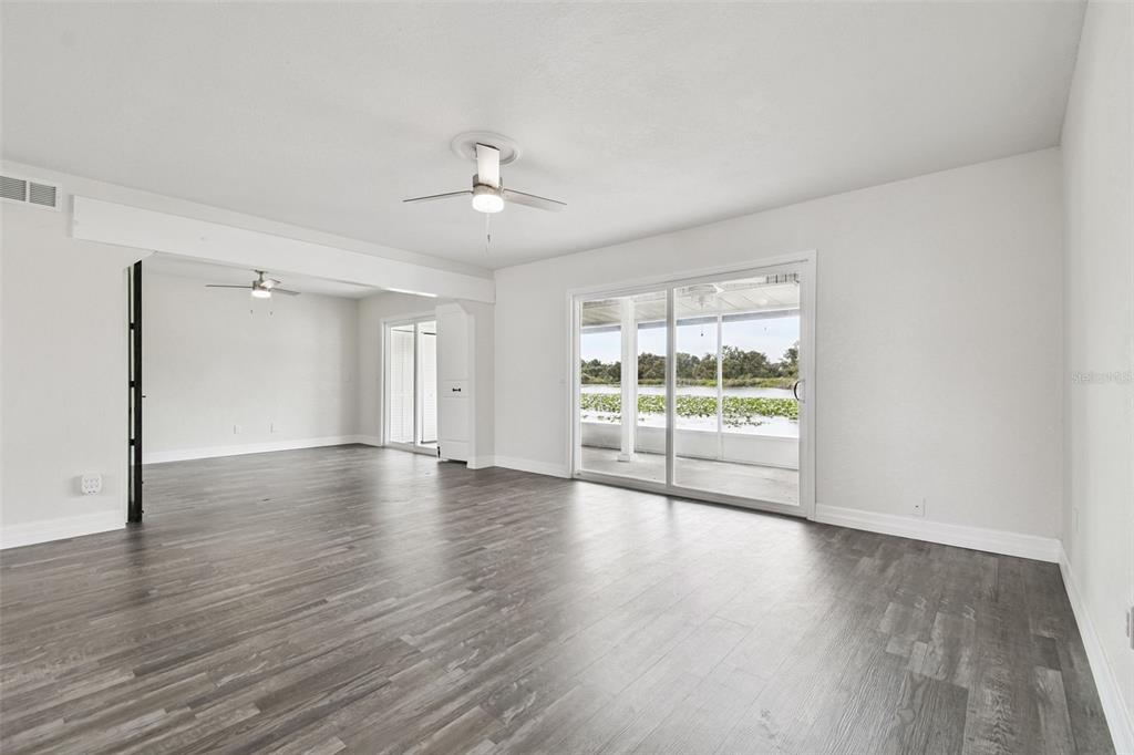 A bright living room features gray wood-look flooring, ceiling fans, and sliding glass doors — 4036 CORTEZ DRIVE UNIT A, TAMPA, FL