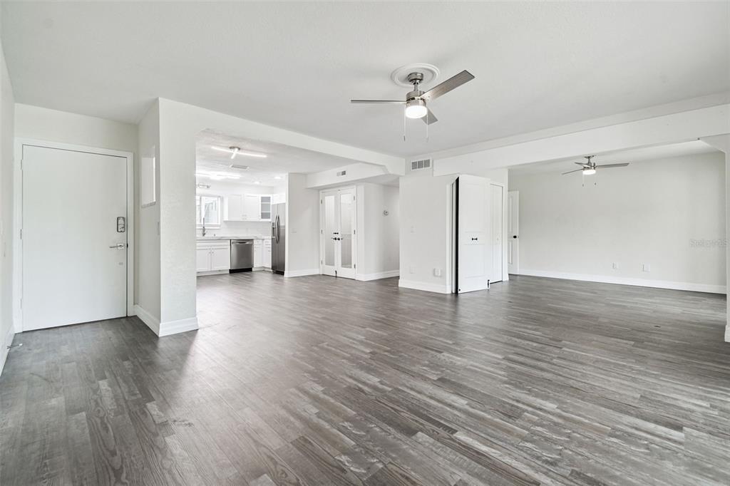 An open-concept living area with gray wood-look flooring, white walls, and a kitchen in back — 4036 CORTEZ DRIVE UNIT A, TAMPA, FL