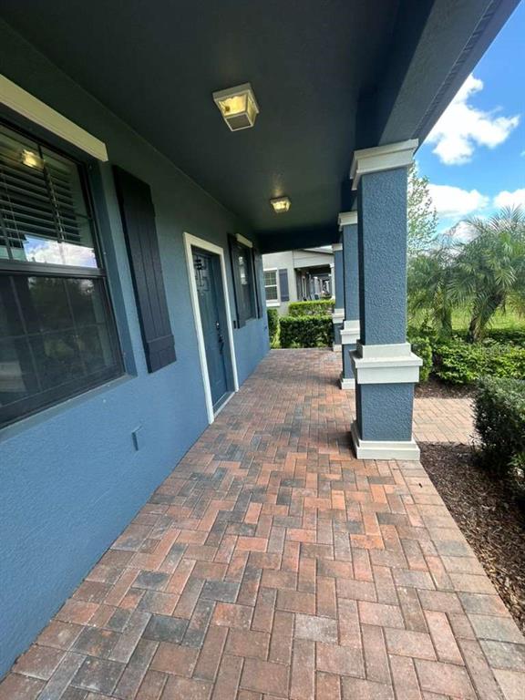 A covered porch features blue exterior walls, a brick paver floor, and white-trimmed columns — 4609 BEXLEY VILLAGE DRIVE, LAND O LAKES, FL