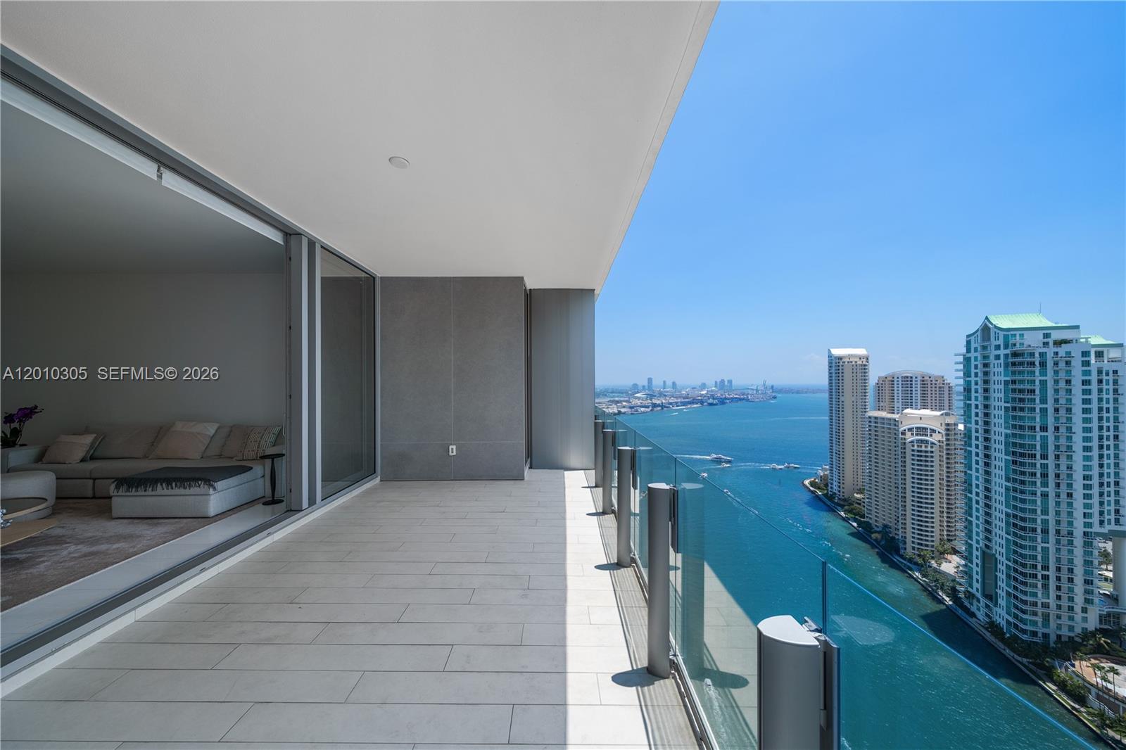 A high-rise balcony features light tile flooring, a glass railing, and expansive water views — 300 Biscayne Blvd Way # 3503C, Miami FL 33131, MIAMI, FL