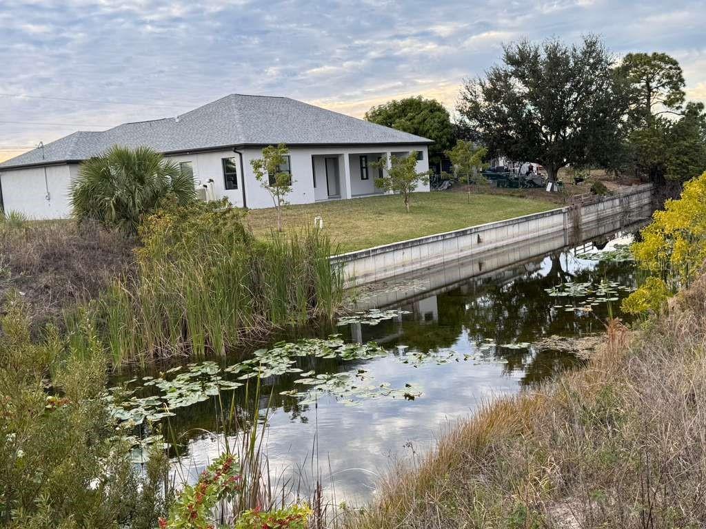 A white house with a gray roof sits behind a canal with lily pads — 1302 NE 19TH PLACE, CAPE CORAL, FL