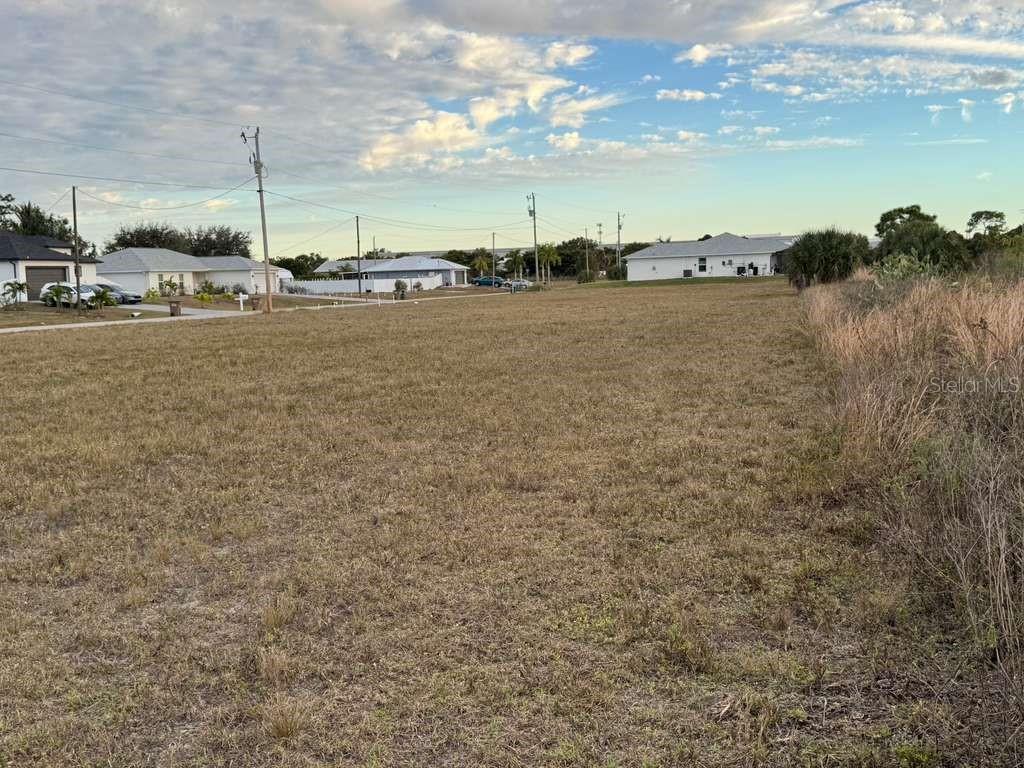 A vacant, grassy residential lot sits in a suburban neighborhood under a cloudy sky — 1302 NE 19TH PLACE, CAPE CORAL, FL