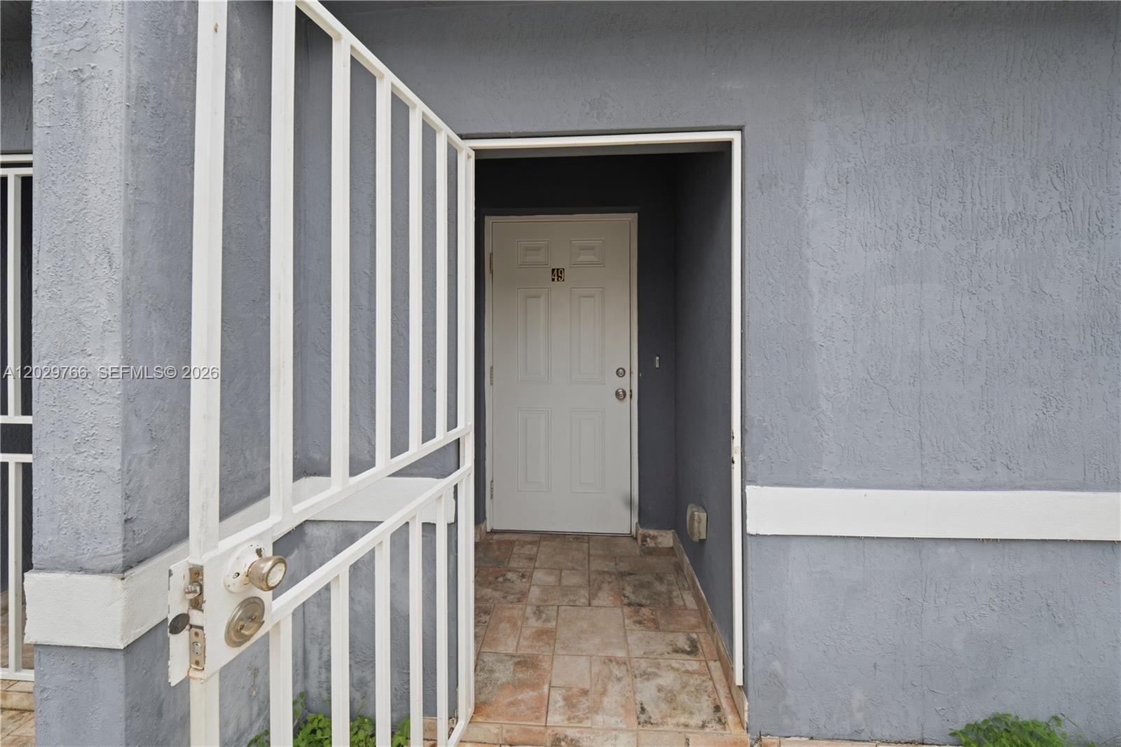 A white security gate opens to a tiled entryway leading to a white front door — 2249/2251 NW 66th St, Miami FL 33147, MIAMI, FL