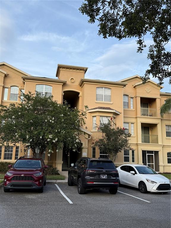 A three-story tan apartment building stands behind a parking lot with three parked cars — 714 TERRACE RIDGE CIRCLE UNIT 714, DAVENPORT, FL