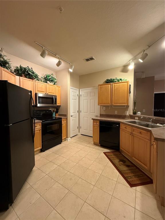 A kitchen features light wood cabinets, black appliances, tile flooring, and track lighting — 714 TERRACE RIDGE CIRCLE UNIT 714, DAVENPORT, FL