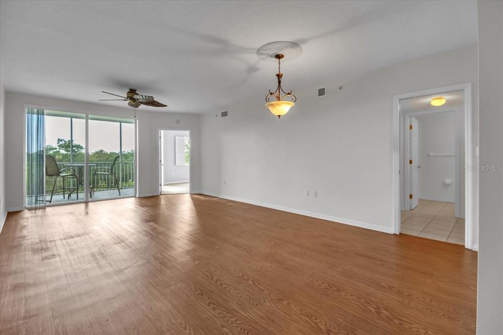 A spacious living room features light wood-look flooring, a ceiling fan, and a balcony view — 2625 TERRA CEIA BAY BOULEVARD UNIT 103, PALMETTO, FL