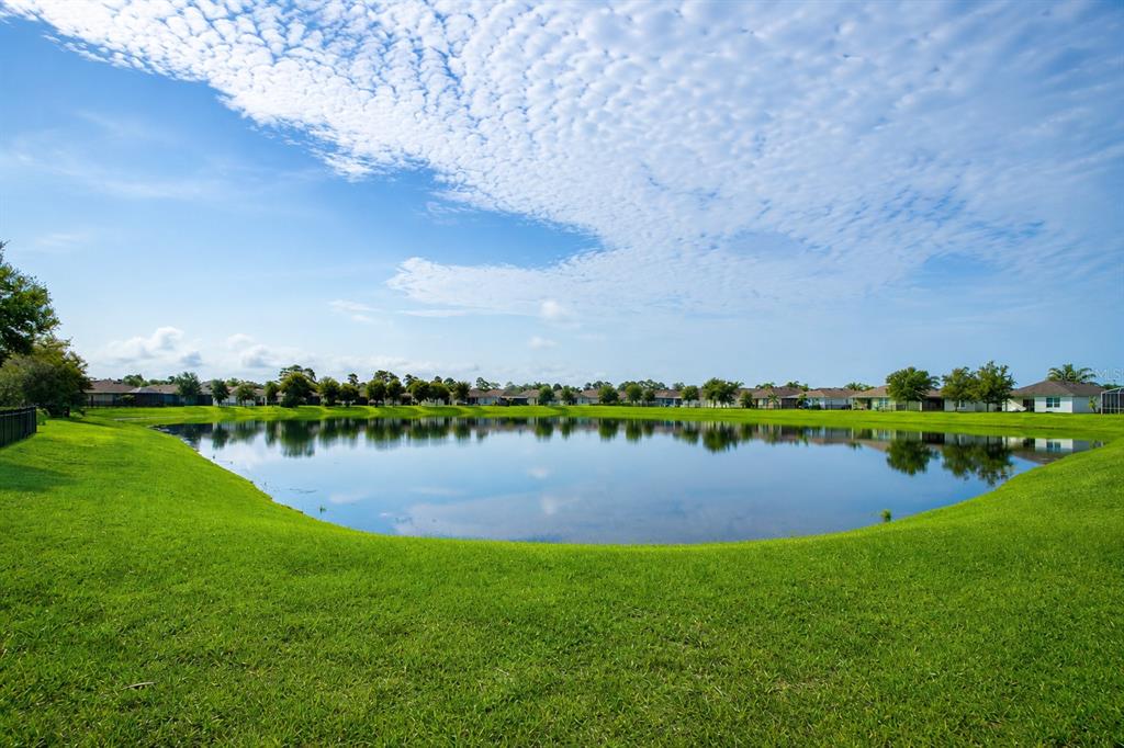A wide, grassy lawn slopes down to a calm pond surrounded by suburban houses — 2989 GIBRALTAR BOULEVARD, NEW SMYRNA BEACH, FL