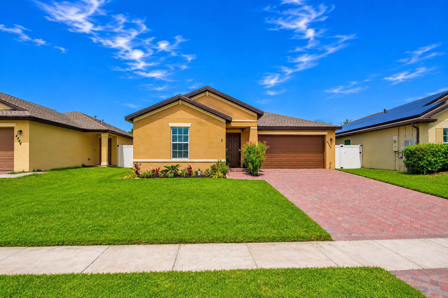 A single-story tan house with a brick driveway and a green lawn under a blue sky — 4242 Thurso Way, Fort Pierce FL 34947, FORT PIERCE, FL