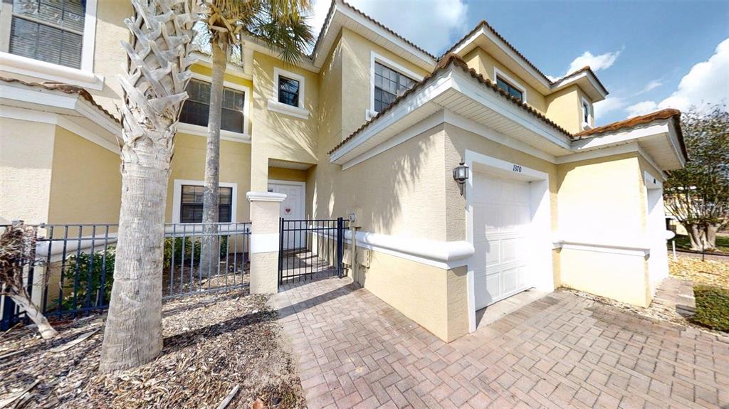 A two-story tan stucco townhouse with a white garage door and a gated entryway — 1370 PACIFIC ROAD, KISSIMMEE, FL