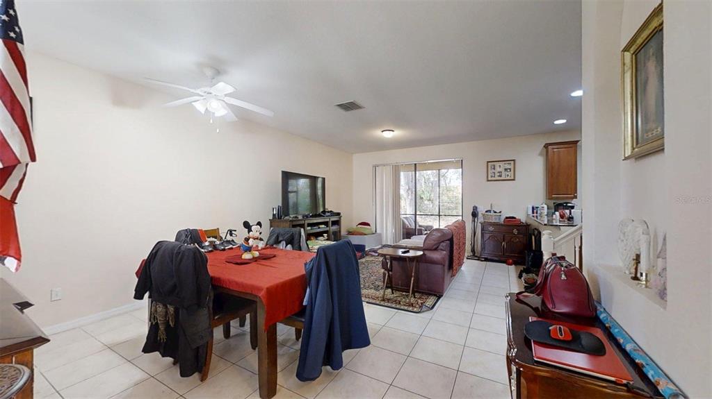 A dining area with a red tablecloth flows into a living room with tile flooring — 1370 PACIFIC ROAD, KISSIMMEE, FL