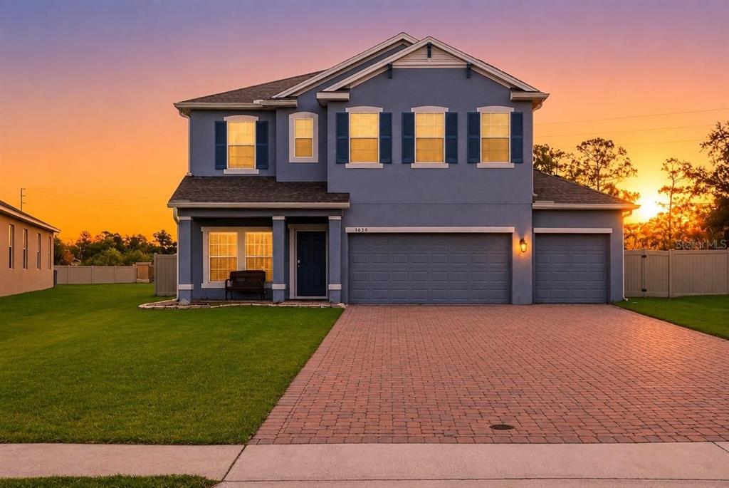 A two-story blue house with a brick paver driveway and a three-car garage at sunset — 3830 SPIRITED CIRCLE, ST CLOUD, FL