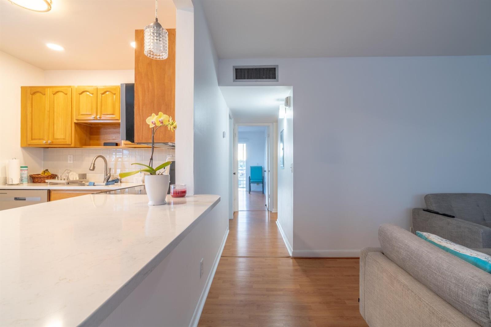 A kitchen with light wood cabinets and a white countertop overlooks a hallway and living area — 313 Burgundy G, Delray Beach FL 33484, DELRAY BEACH, FL
