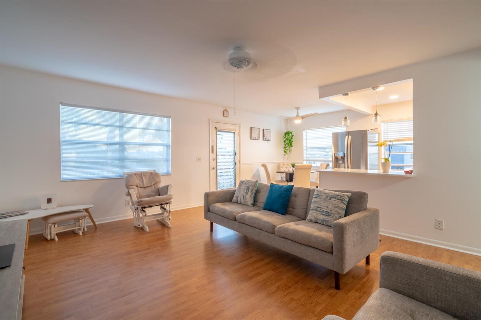 A living room with light wood floors, a gray sofa, and an open kitchen area — 313 Burgundy G, Delray Beach FL 33484, DELRAY BEACH, FL