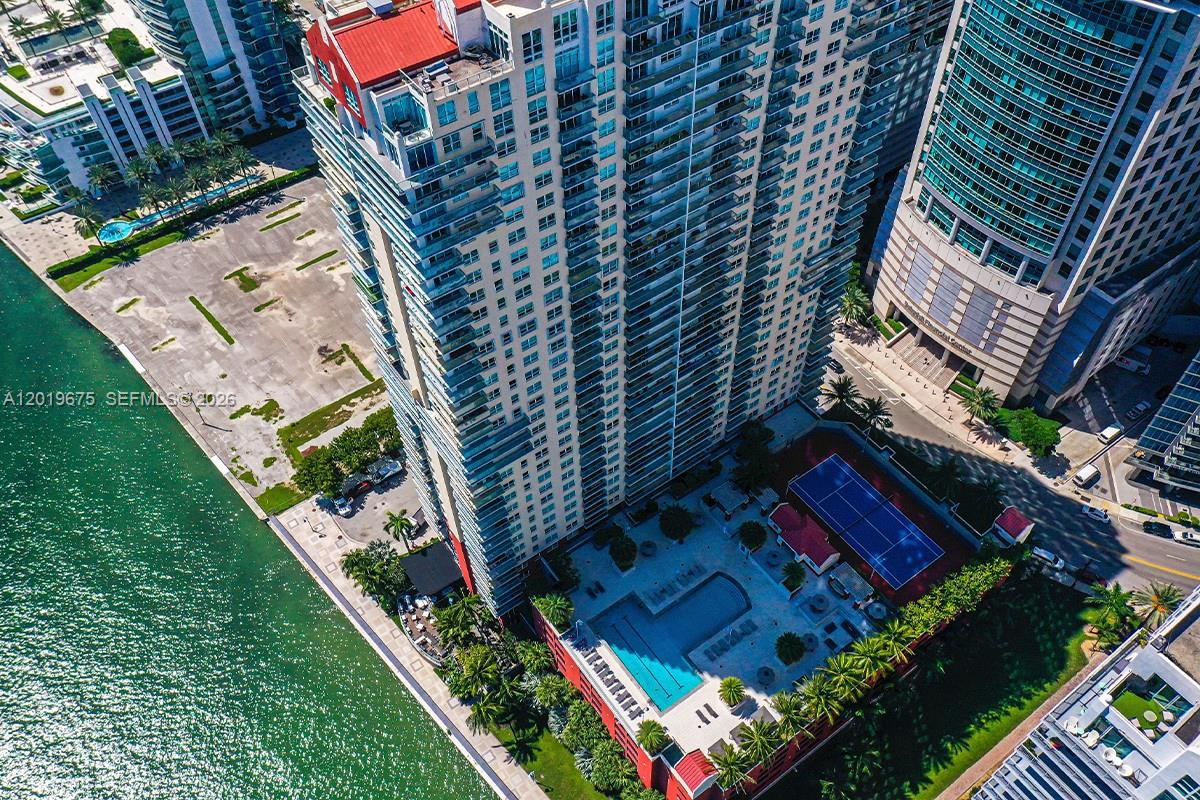An aerial view shows a tall residential building with a pool, tennis court, and waterfront — 1155 Brickell Bay Dr # 1205, Miami FL 33131, MIAMI, FL