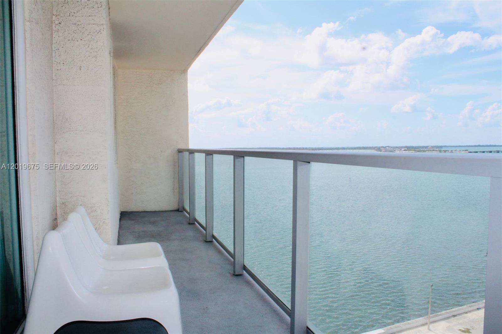 A balcony with white chairs overlooks a large body of water under a cloudy sky — 1155 Brickell Bay Dr # 1205, Miami FL 33131, MIAMI, FL
