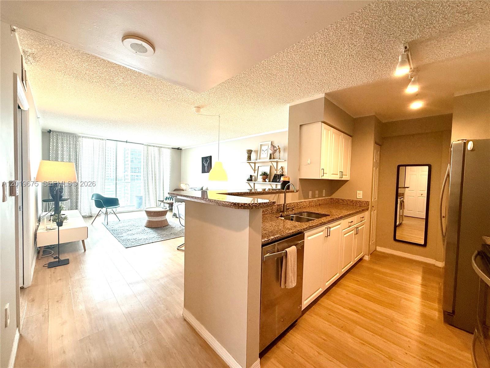 An open-concept kitchen with granite countertops overlooks a living area with floor-to-ceiling windows — 1155 Brickell Bay Dr # 1205, Miami FL 33131, MIAMI, FL