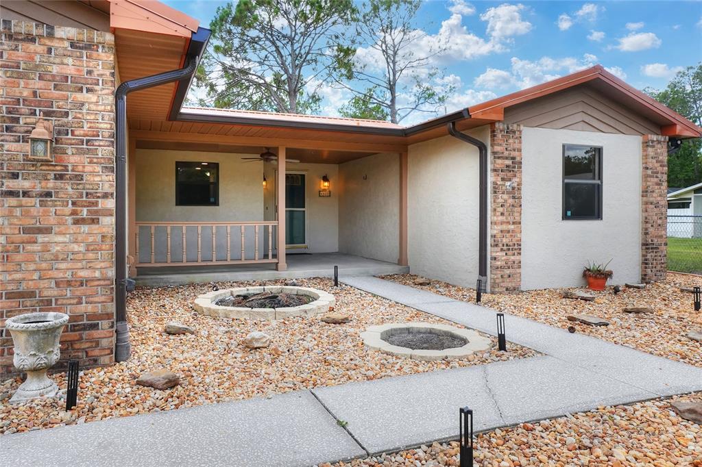 A house exterior features a covered porch, a stone fire pit, and a gravel yard — 4520 LOG CABIN DRIVE, LAKELAND, FL