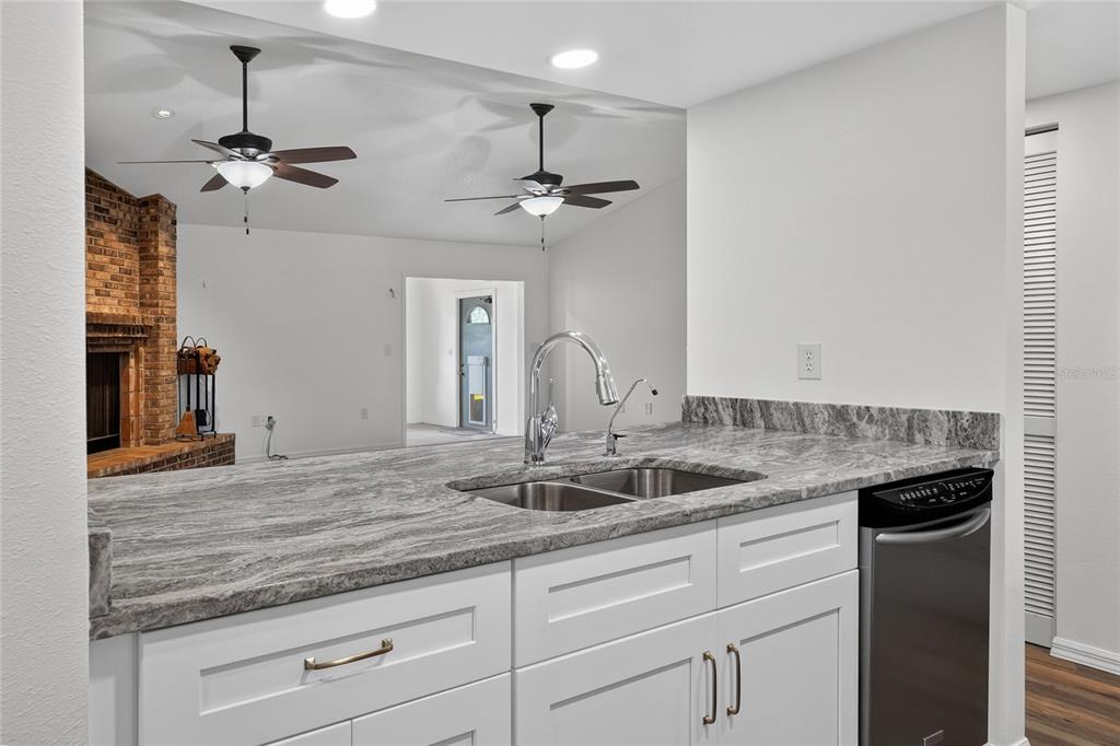 A kitchen sink with a granite countertop and white cabinets overlooks a living area — 4520 LOG CABIN DRIVE, LAKELAND, FL