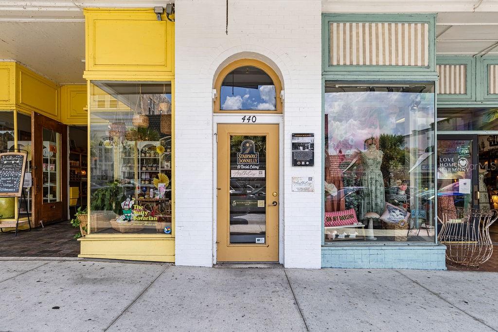 The exterior of a storefront building features a central door flanked by yellow and teal windows — 440 N DONNELLY STREET, MOUNT DORA, FL