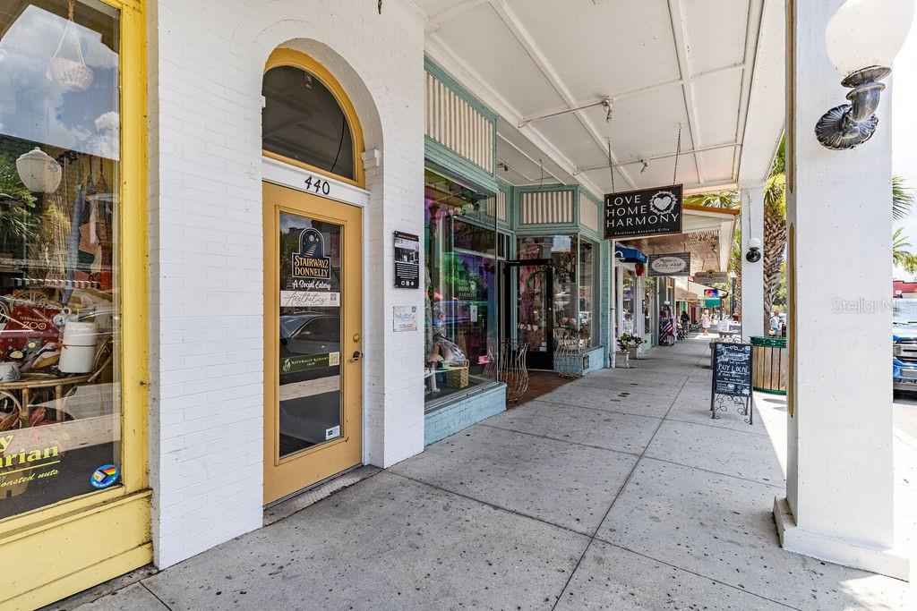 A sidewalk leads past storefronts with arched doorways, large display windows, and hanging business signs — 440 N DONNELLY STREET, MOUNT DORA, FL