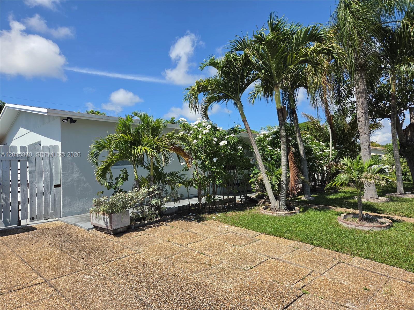 A white house exterior features a wooden gate, palm trees, and a paved driveway — 140 NW 18th St, Pompano Beach FL 33060, POMPANO BEACH, FL