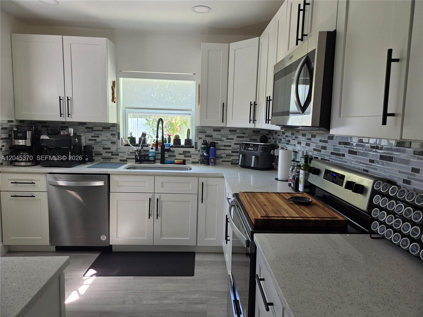A kitchen features white cabinets, stainless steel appliances, quartz countertops, and a gray tiled backsplash — 140 NW 18th St, Pompano Beach FL 33060, POMPANO BEACH, FL