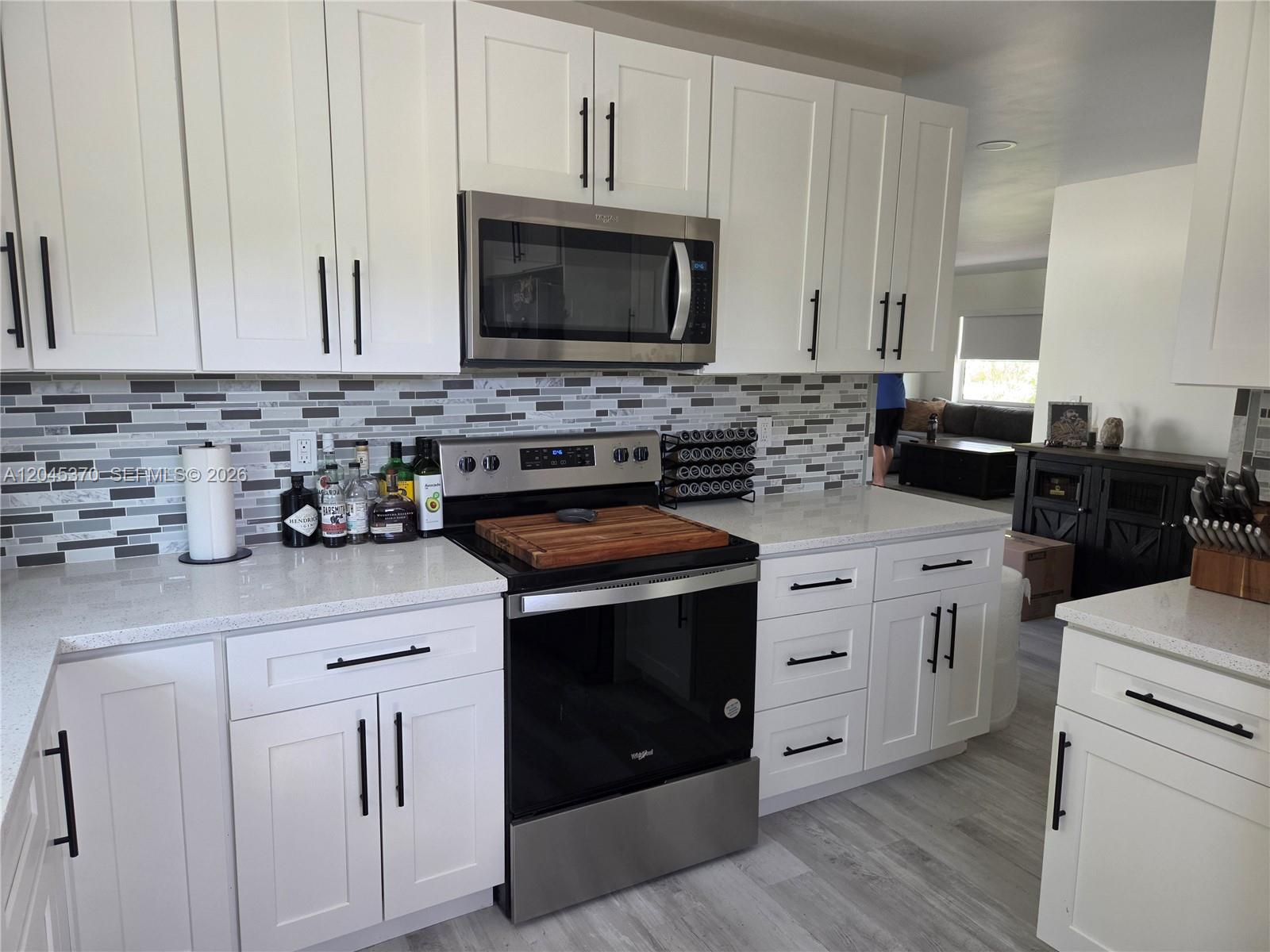 A kitchen features white cabinets, stainless steel appliances, a tiled backsplash, and light-colored countertops — 140 NW 18th St, Pompano Beach FL 33060, POMPANO BEACH, FL