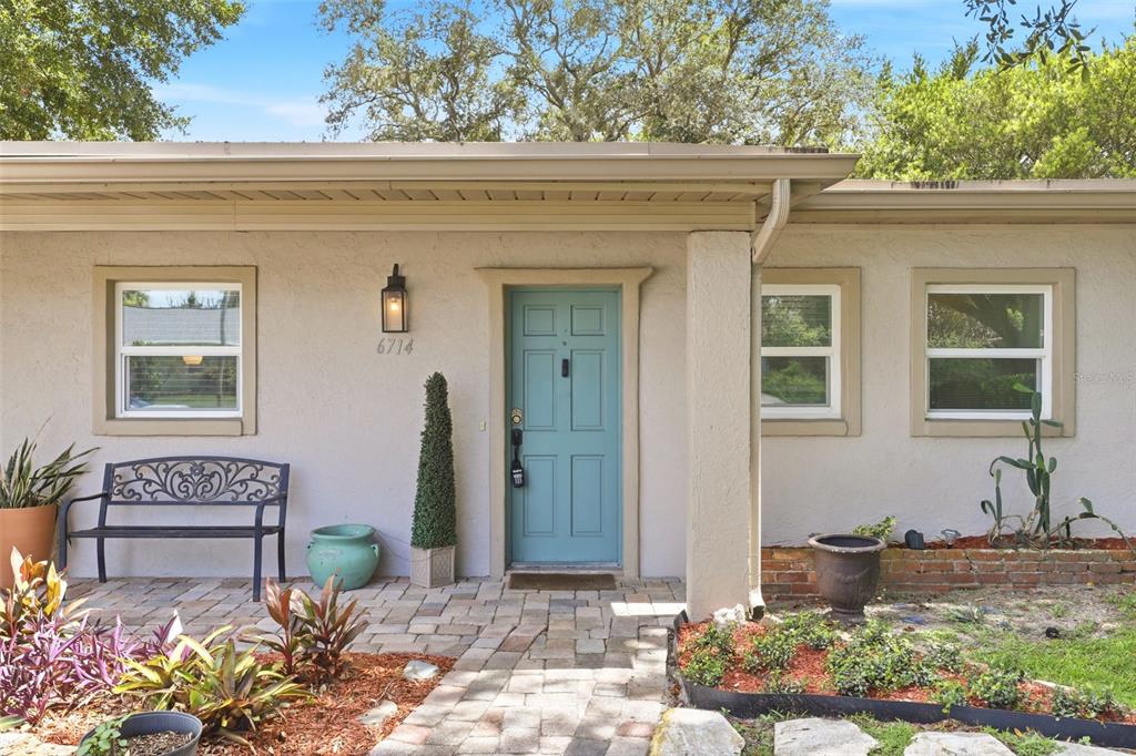 A teal front door is centered on a beige stucco house with a brick walkway — 6714 NINA ROSA DRIVE, ORLANDO, FL