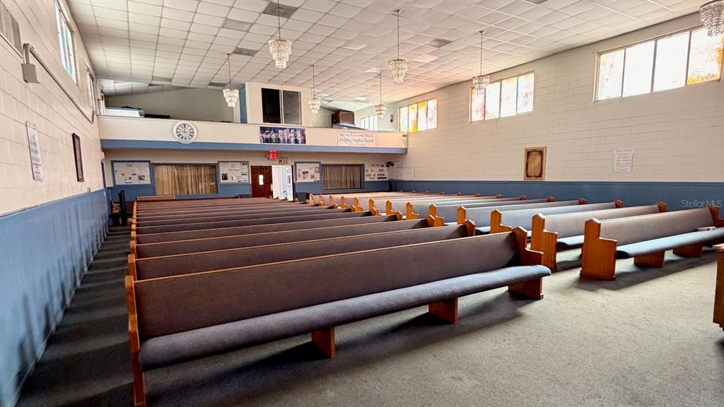 An interior view of a church sanctuary featuring rows of wooden pews and hanging chandeliers — 514 S PARRAMORE AVENUE, ORLANDO, FL