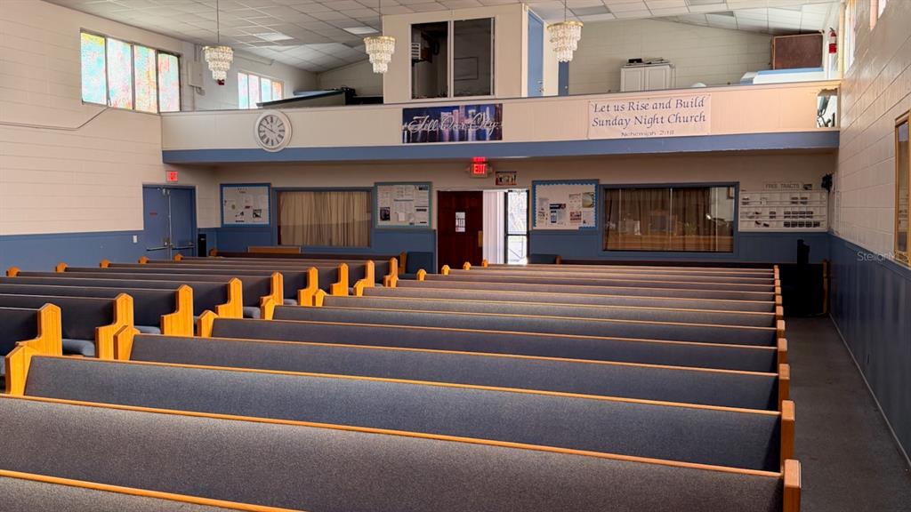 A church sanctuary features rows of blue upholstered pews facing a rear wall with windows — 514 S PARRAMORE AVENUE, ORLANDO, FL