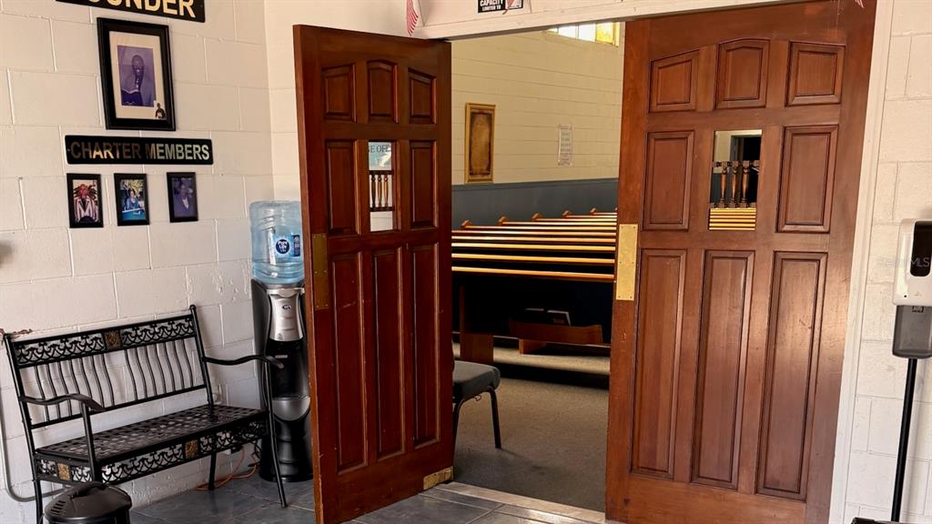 A wooden double door opens into a church sanctuary with rows of wooden pews — 514 S PARRAMORE AVENUE, ORLANDO, FL
