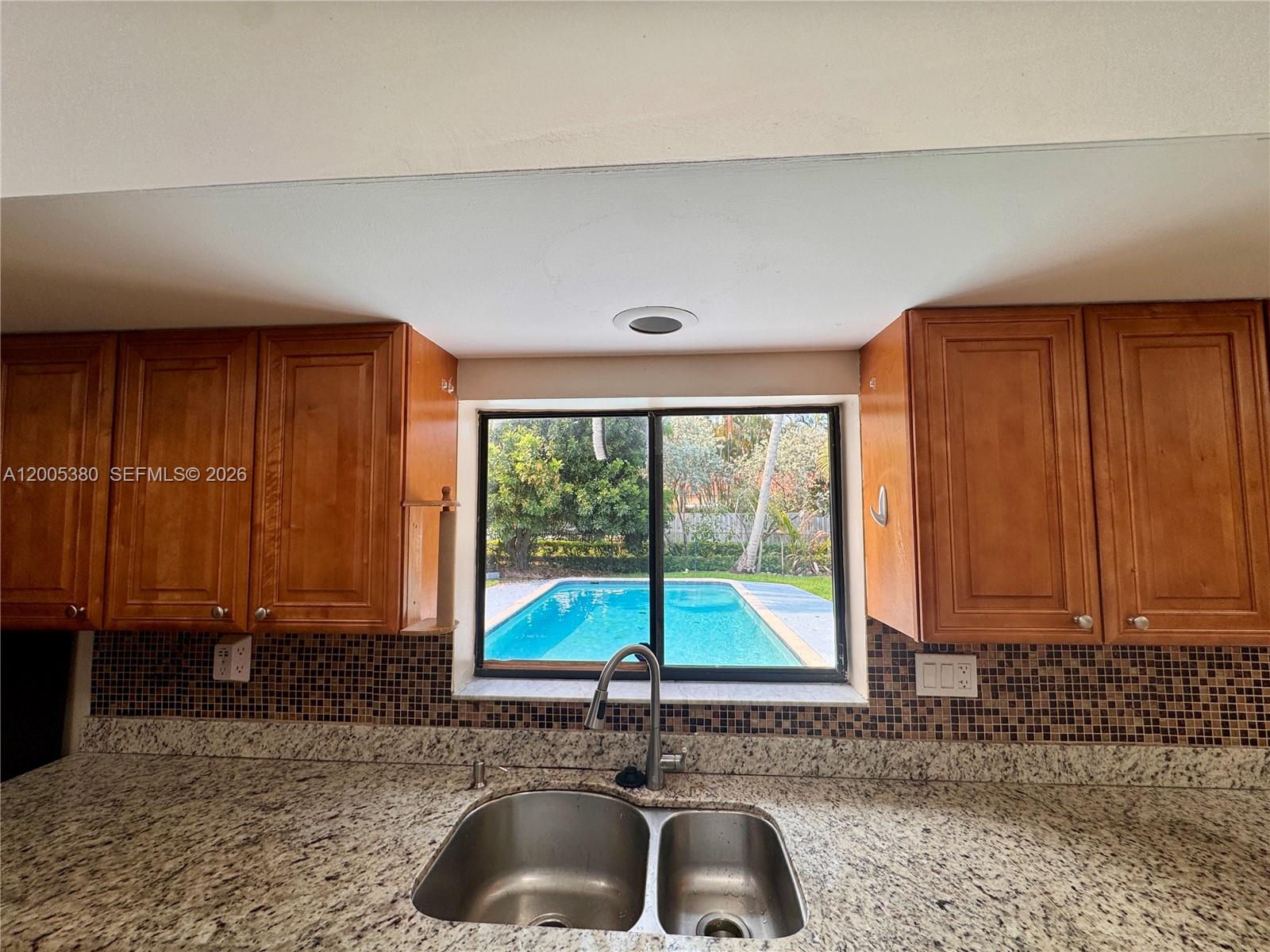 A kitchen sink with granite countertops faces a window overlooking a backyard swimming pool — 13425 NW 10th St, Sunrise FL 33323, SUNRISE, FL