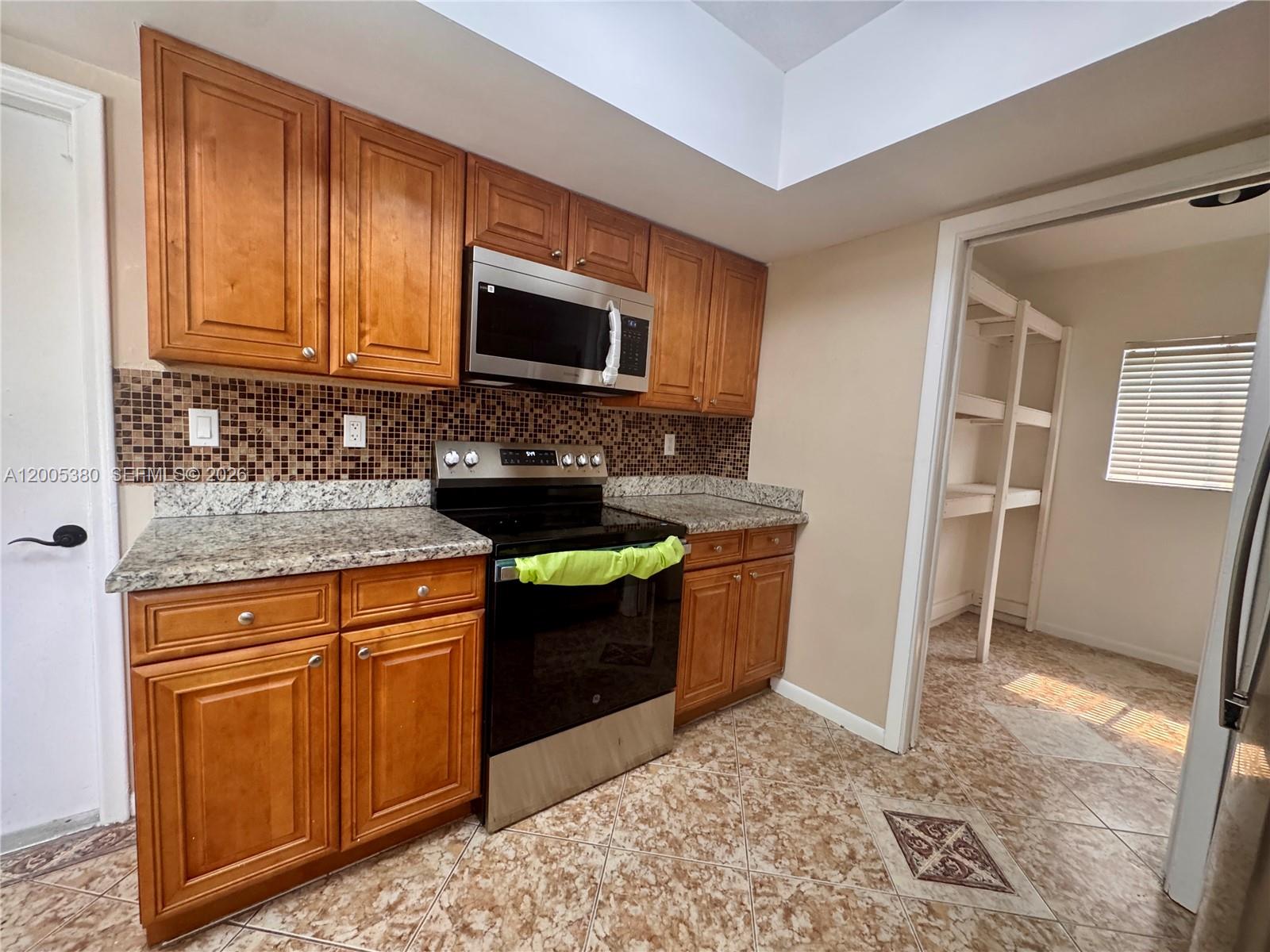 A kitchen features wood cabinets, granite countertops, a tiled backsplash, and a walk-in pantry — 13425 NW 10th St, Sunrise FL 33323, SUNRISE, FL